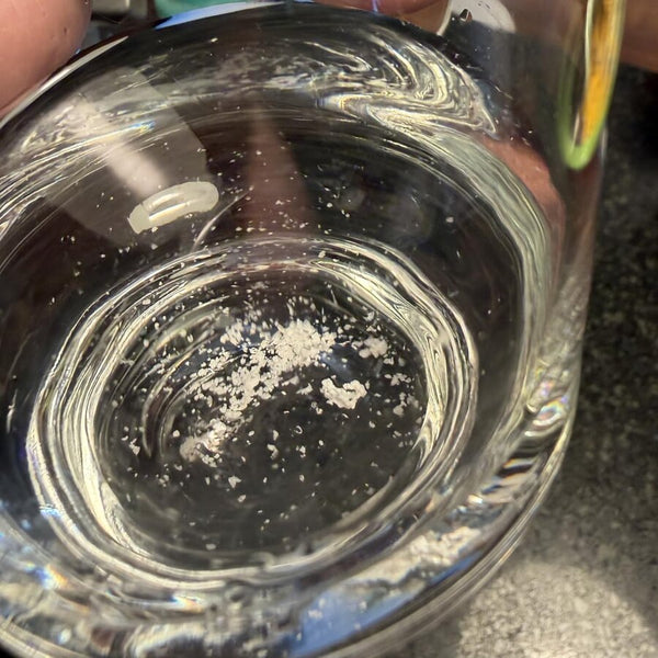 Des flocons de minéraux blancs au fond d’un verre d’eau